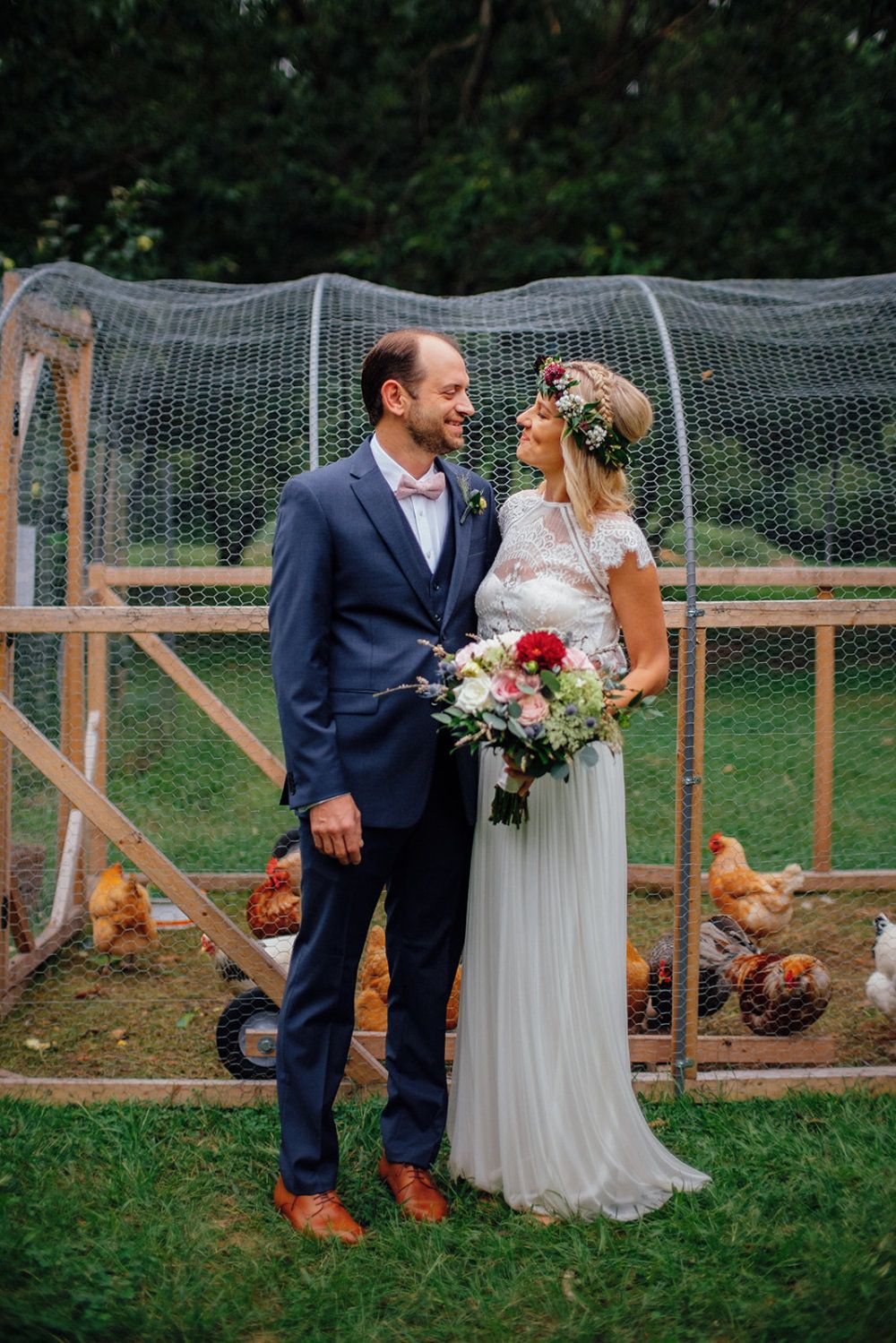 On their wedding day, a couple smiles at each other in front of the chicken run.