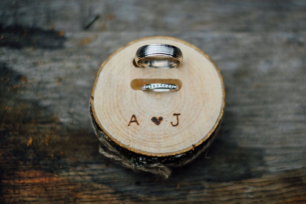 A wooden ring box holds two wedding rings and says "A ? J."