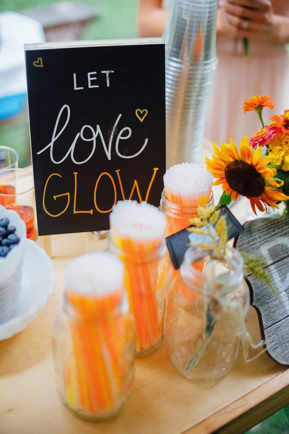 A chalkboards sign that reads "Let Love Glow" is set on a table with Mason Jars of glow sticks.