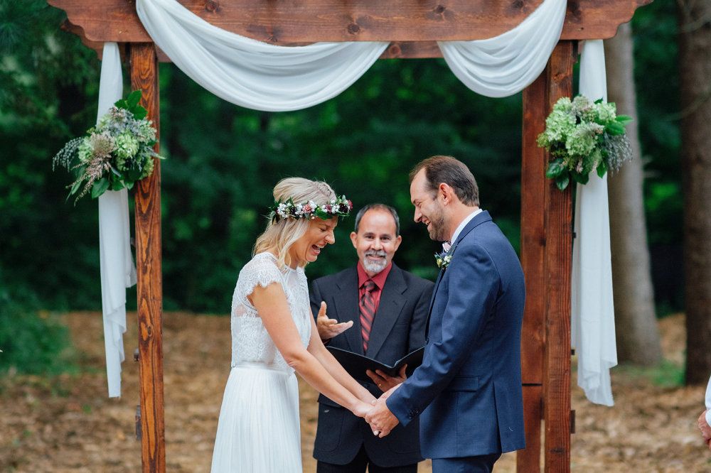 During a wedding ceremony, a couple laughs at what the clergy says.