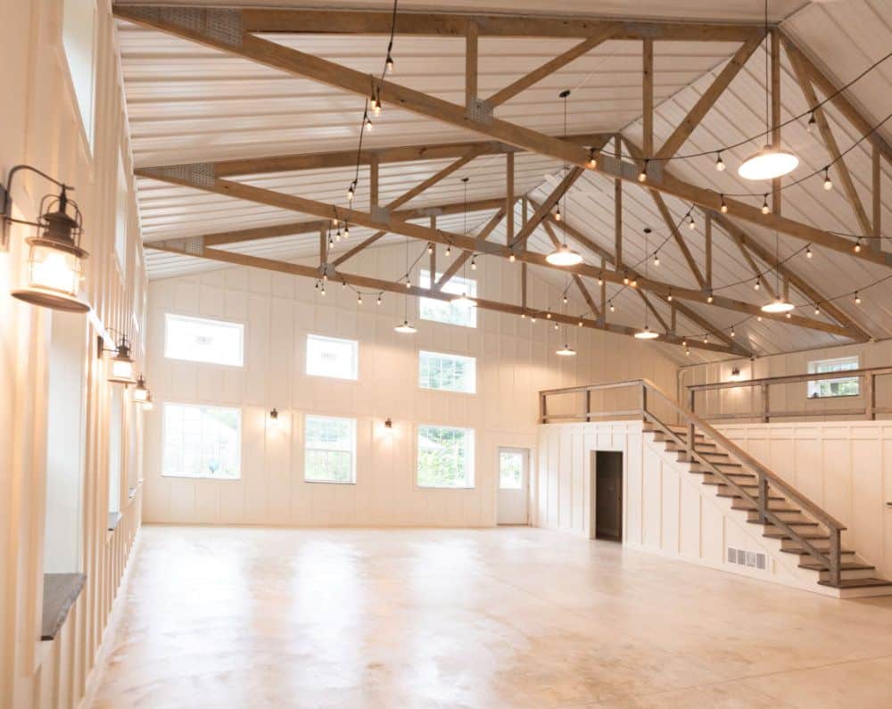 A view from the floor of the barn, showing its white walls, high ceilings, rustic rafters and rails, wide windows, and concrete floor.