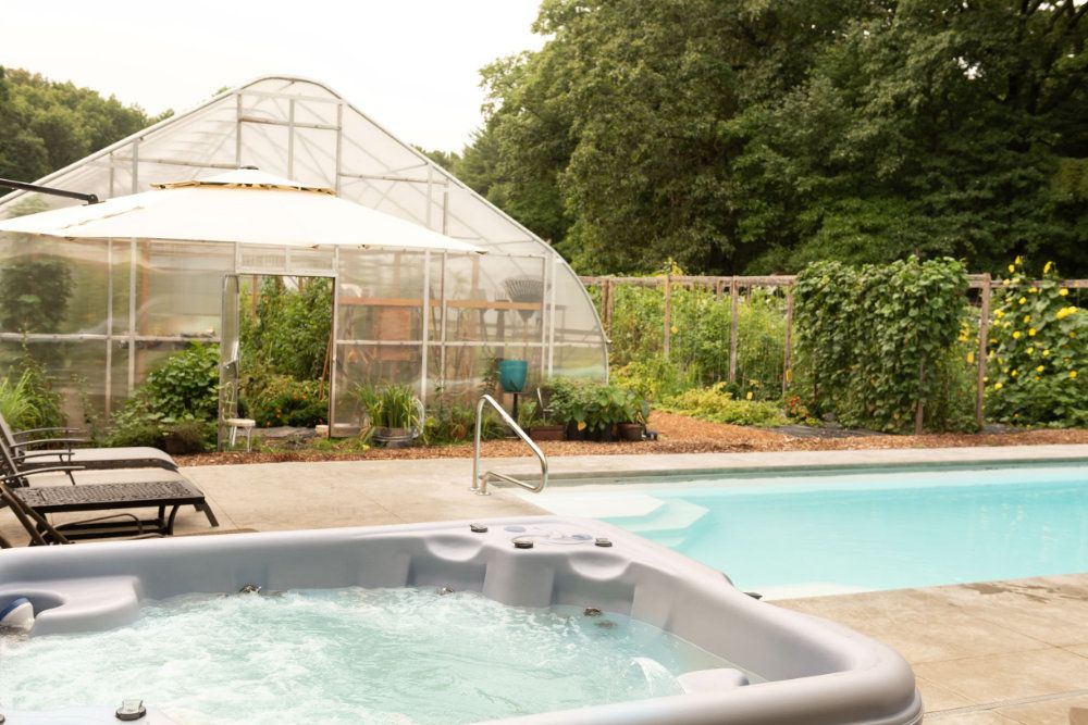 The hot tub and pool overlook the hoophouse and organic garden.