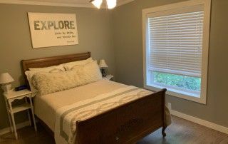 This bedroom has a full sized bed paired with two nightstands. There is a painting above the bed and a large window.