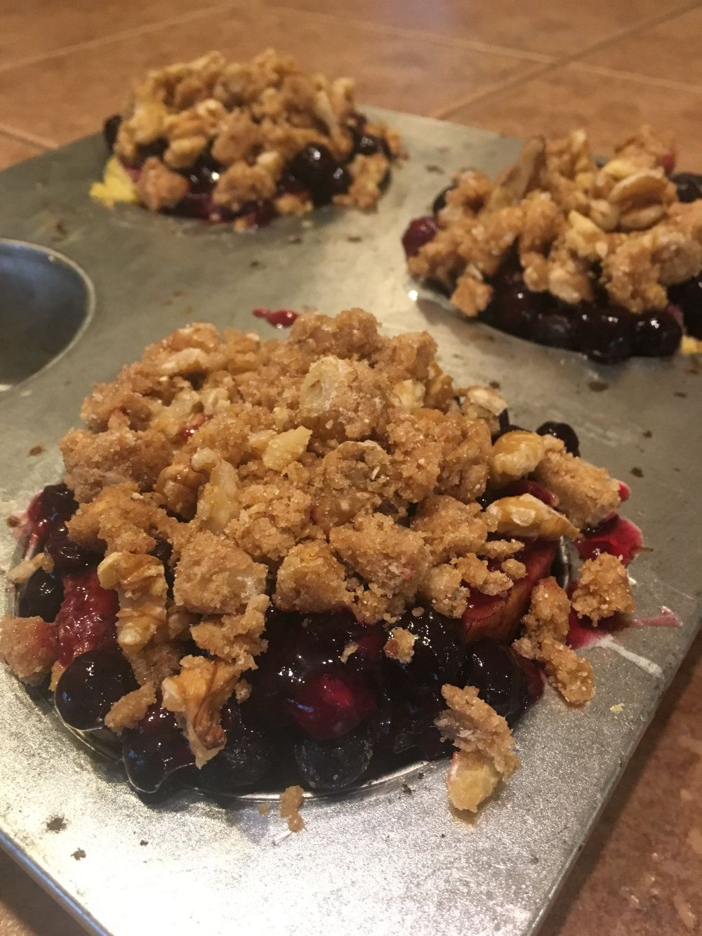 Baked French toast with blueberry compote and sugared nuts are served out of a muffin tin.