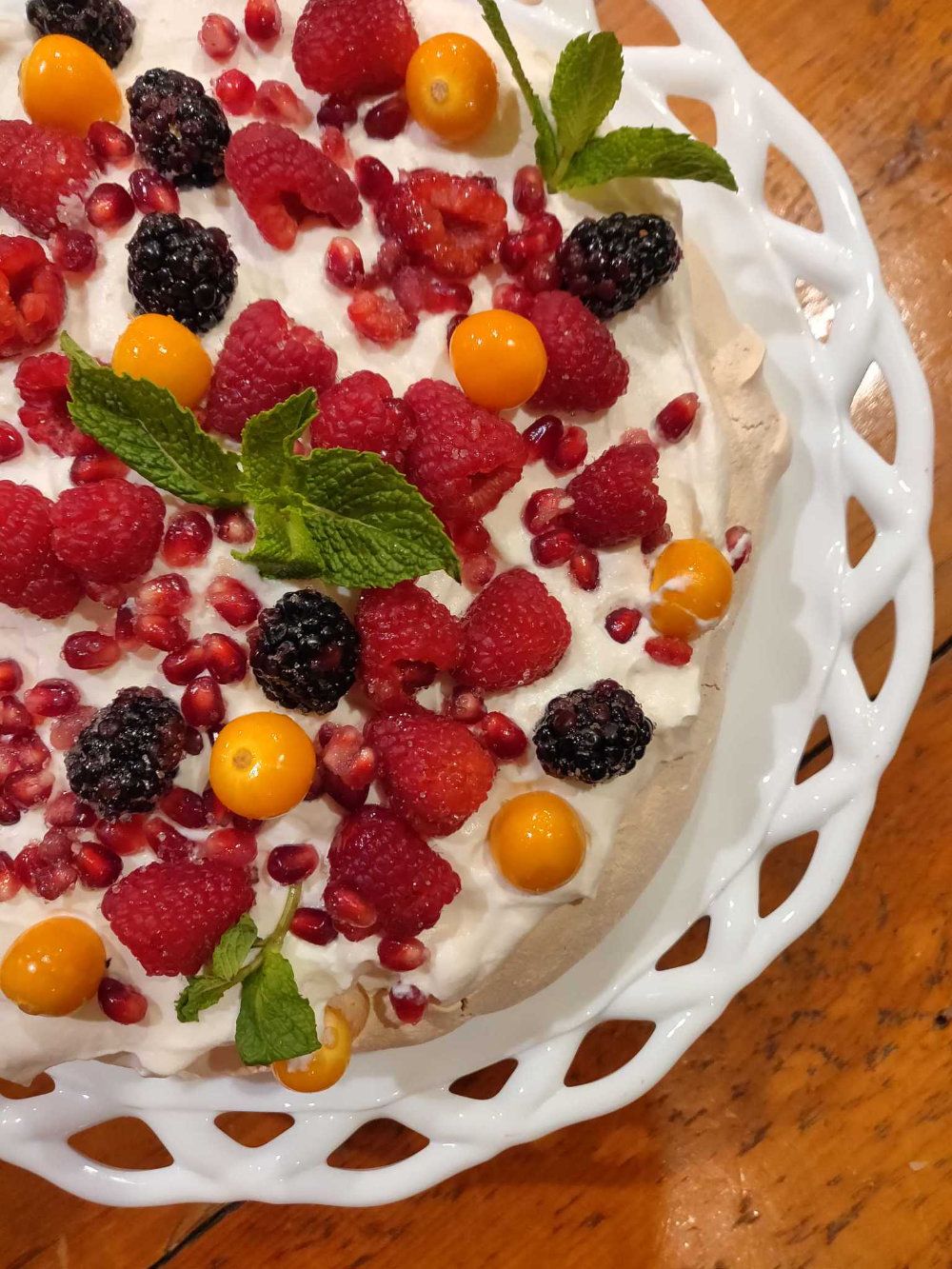 Pavlova topped with raspberries, blackberries, golden berries, and pomegranate served on a white dish.
