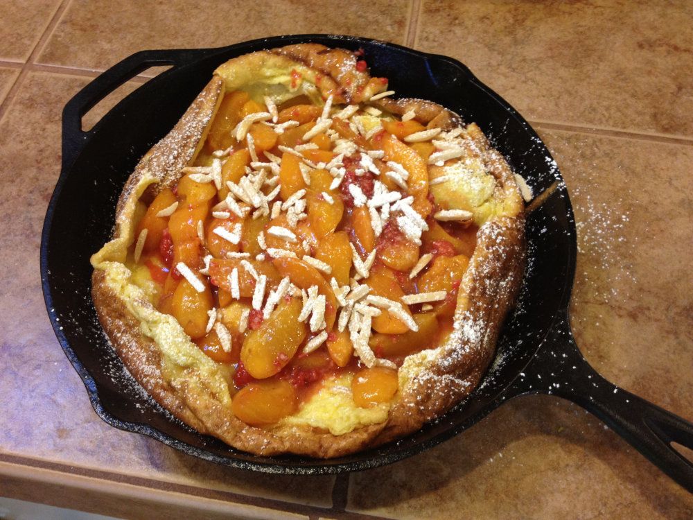 A Dutch baby pancake filled with peaches served in a cast iron skillet.