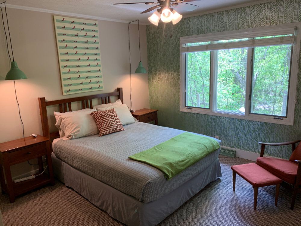 This bedroom includes a queen sized bed, a pair of nightstands, hanging lights, and a comfortable lounge chair.