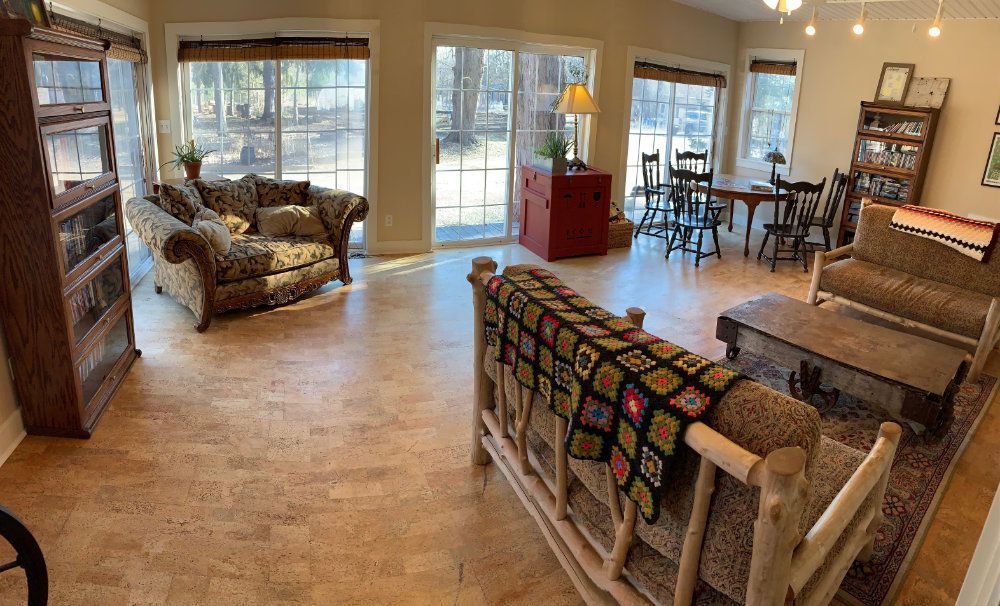 Wide angle view of the Sunroom. Three couches, a coffee table, two book cases full of movies, and a puzzle table can be seen.