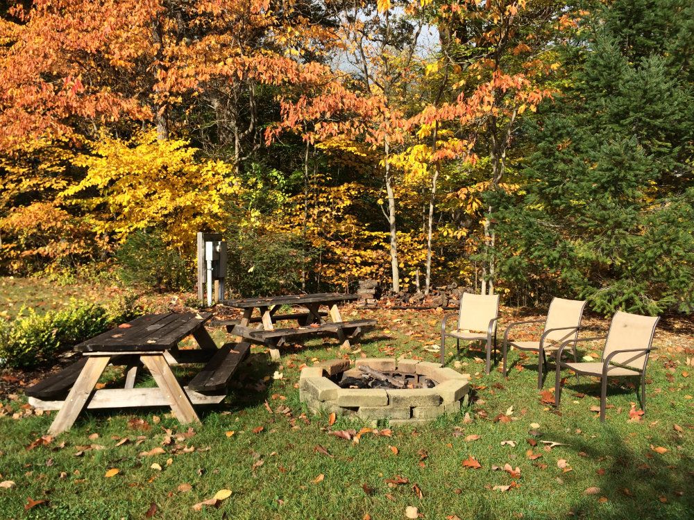 The beautiful outdoor space at Creekside Cottage includes a fire pit, chairs, a picnic bench, and grill.