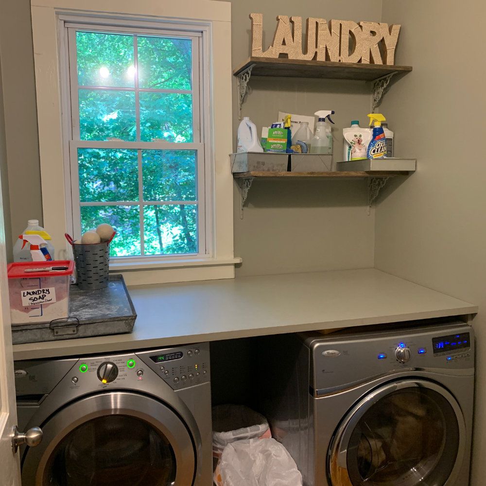 Full sized washer and dryer, folding table, and cleaning supplies are shown in the laundry room.