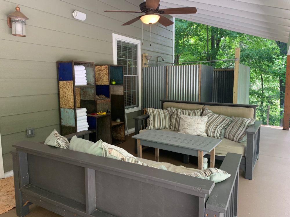 The side yard seating area has two day bed couches, a coffee table, and shelves. In the background, the private outdoor shower can be seen.