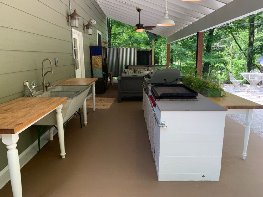 The outdoor kitchen provides plenty of large counter space. There is a full sized grill, flatop grill, and sink. In the background, the seating area can be seen.
