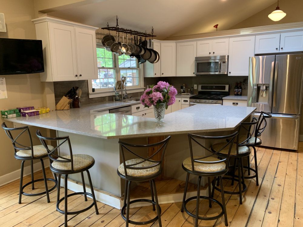 Countertop seating around the edge of the kitchen allows for guests to get an up-close breakfast experience. Hanging pots and pans, a tv, and other kitchen essentials can be seen in the background.