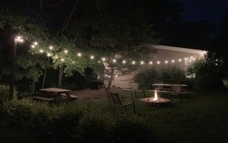 Outdoor space at Creekside Cottage at night. String lights light up the space along with the firepit.