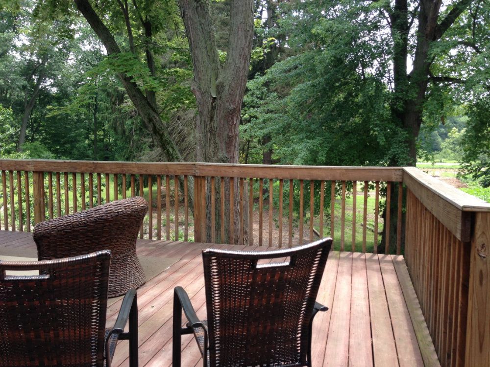 View of upstairs patio from the American Hornbeam room. Three brown deck chairs are pictured looking out onto the gardens.