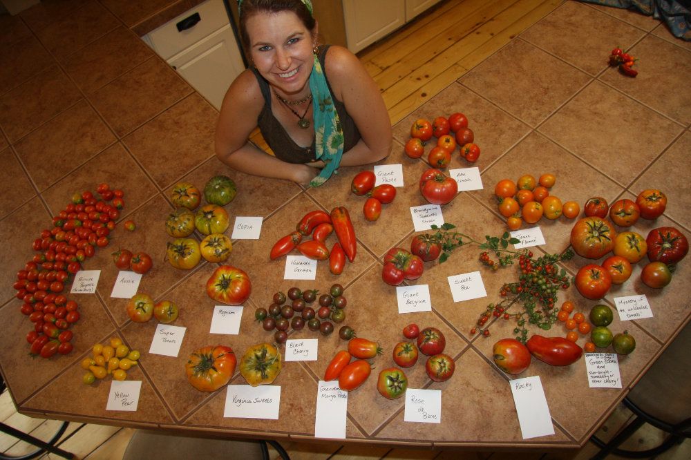 Julie, the innkeeper and head gardener, poses next to a large pile of various labelled tomatoes.