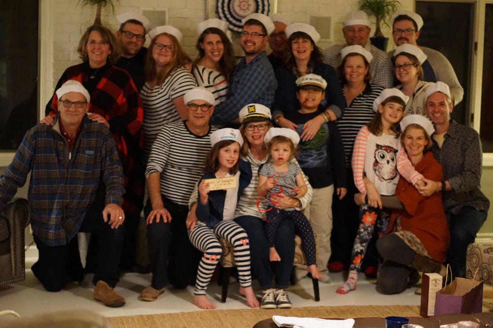 A large group, all wearing sailor's hats, smiles for a picture at the River's Edge living room.