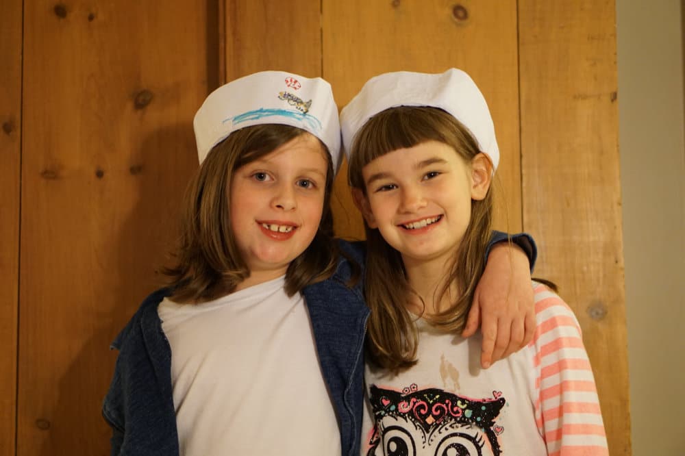 Two kids smile while wearing sailor hats.