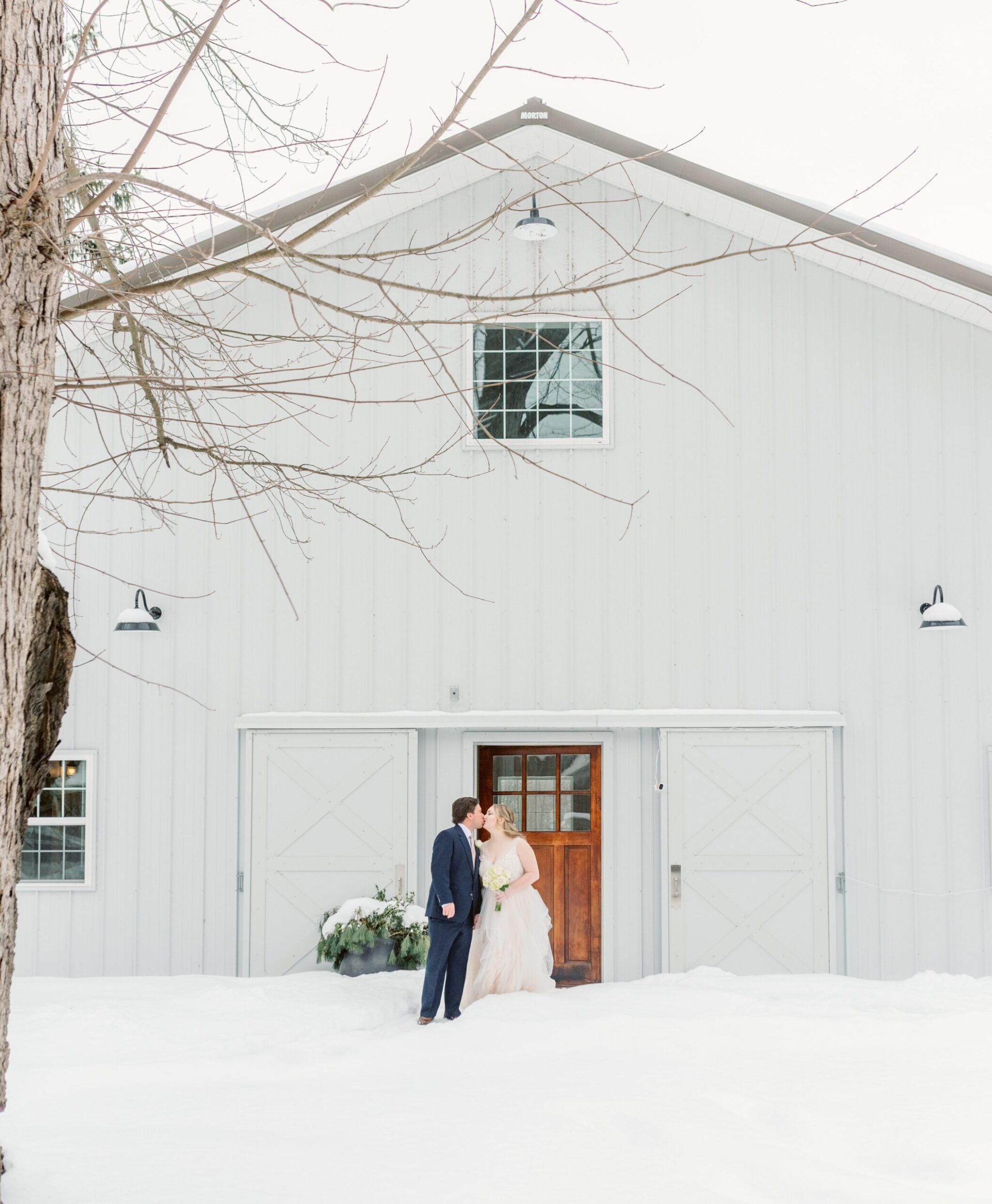 A couple kisses in the snow on their wedding day in front of The Barn.
