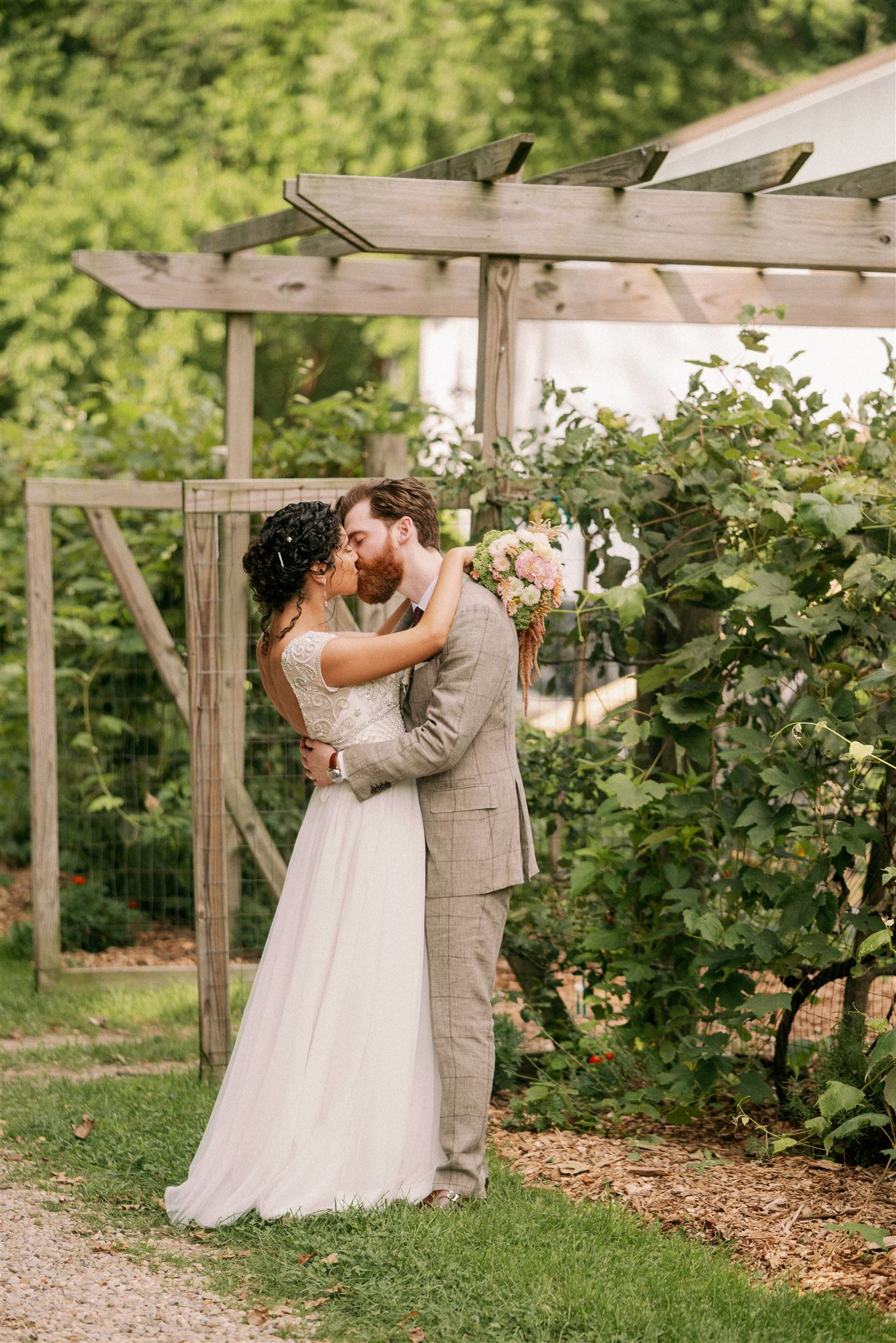 On their wedding day, a couple kisses by the grape vine gates.
