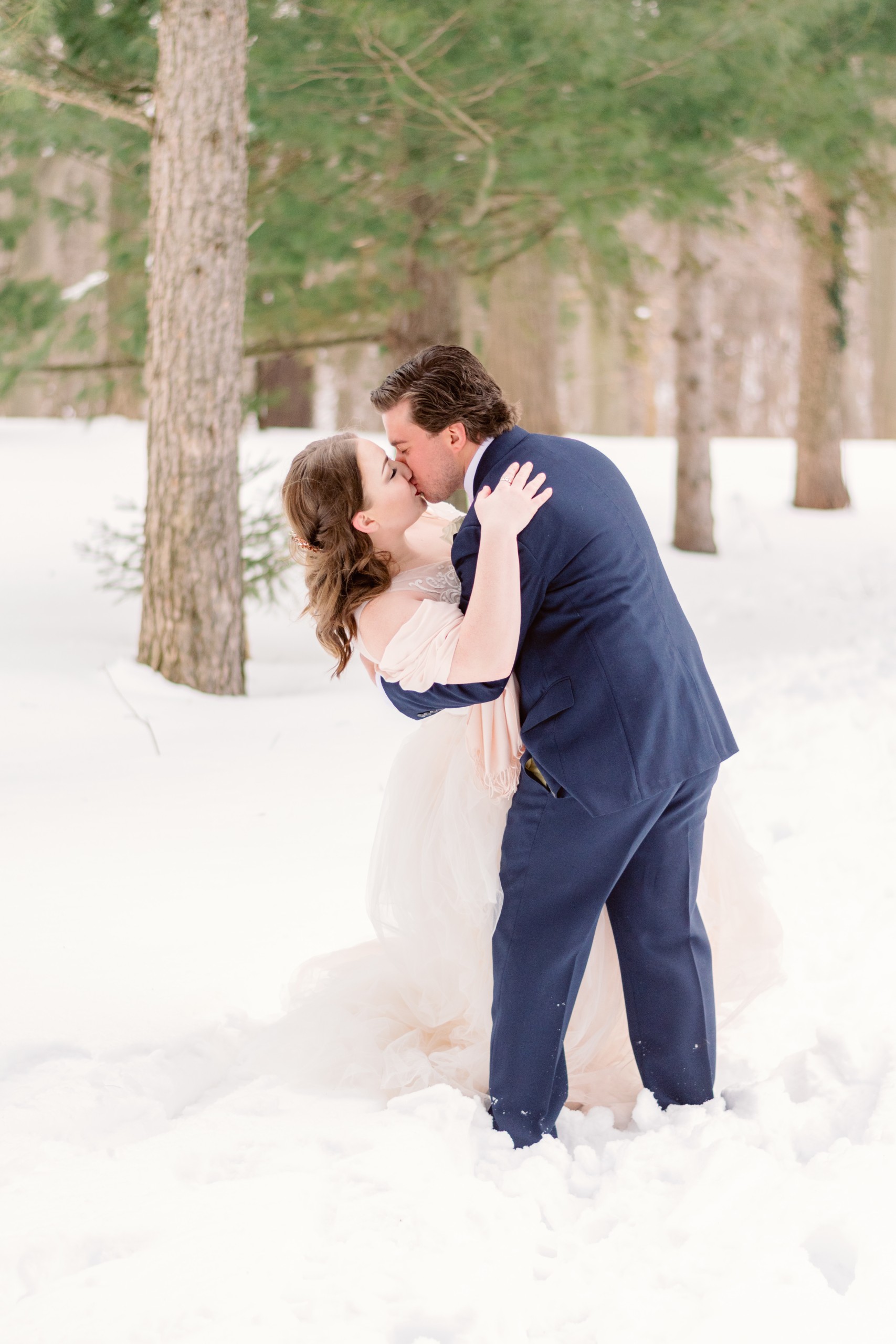A couple kisses in snowy forest on their wedding day.