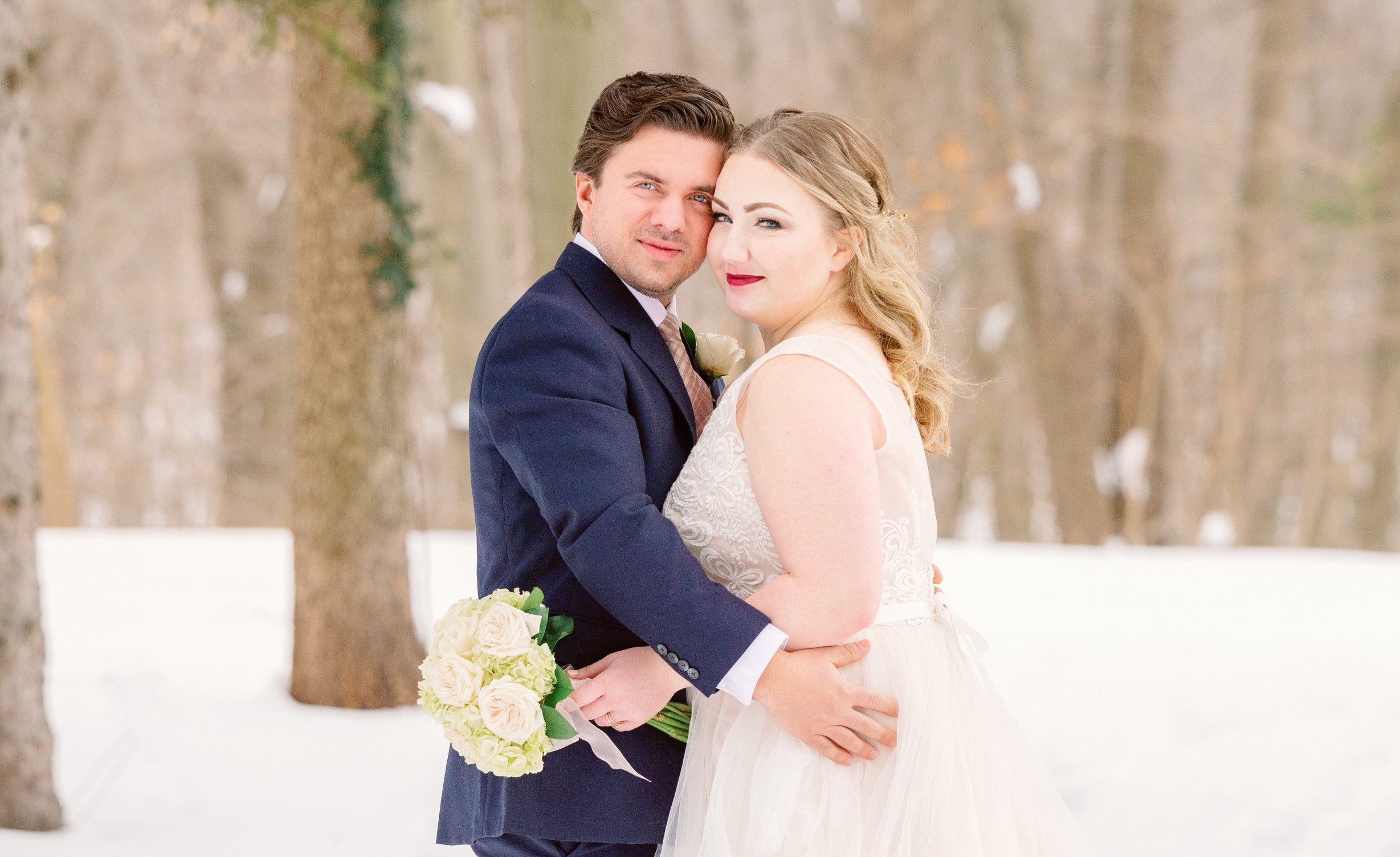 A couple embraces in snowy woods.
