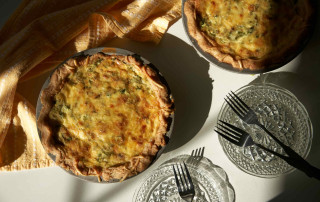 Two quiches, plates, and forks sit on a table is glowing sunlight