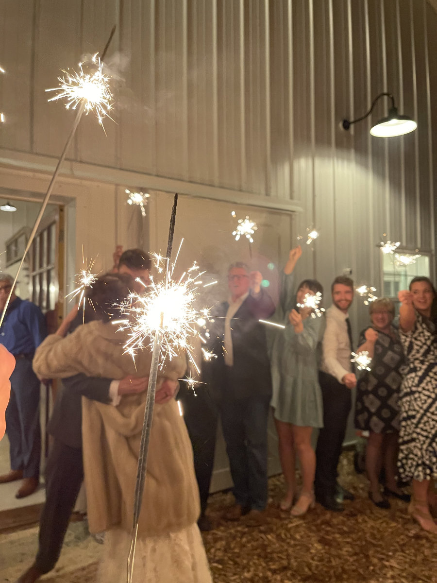 Family and friends celebrate with sparklers outside of the barn as newlyweds kiss.