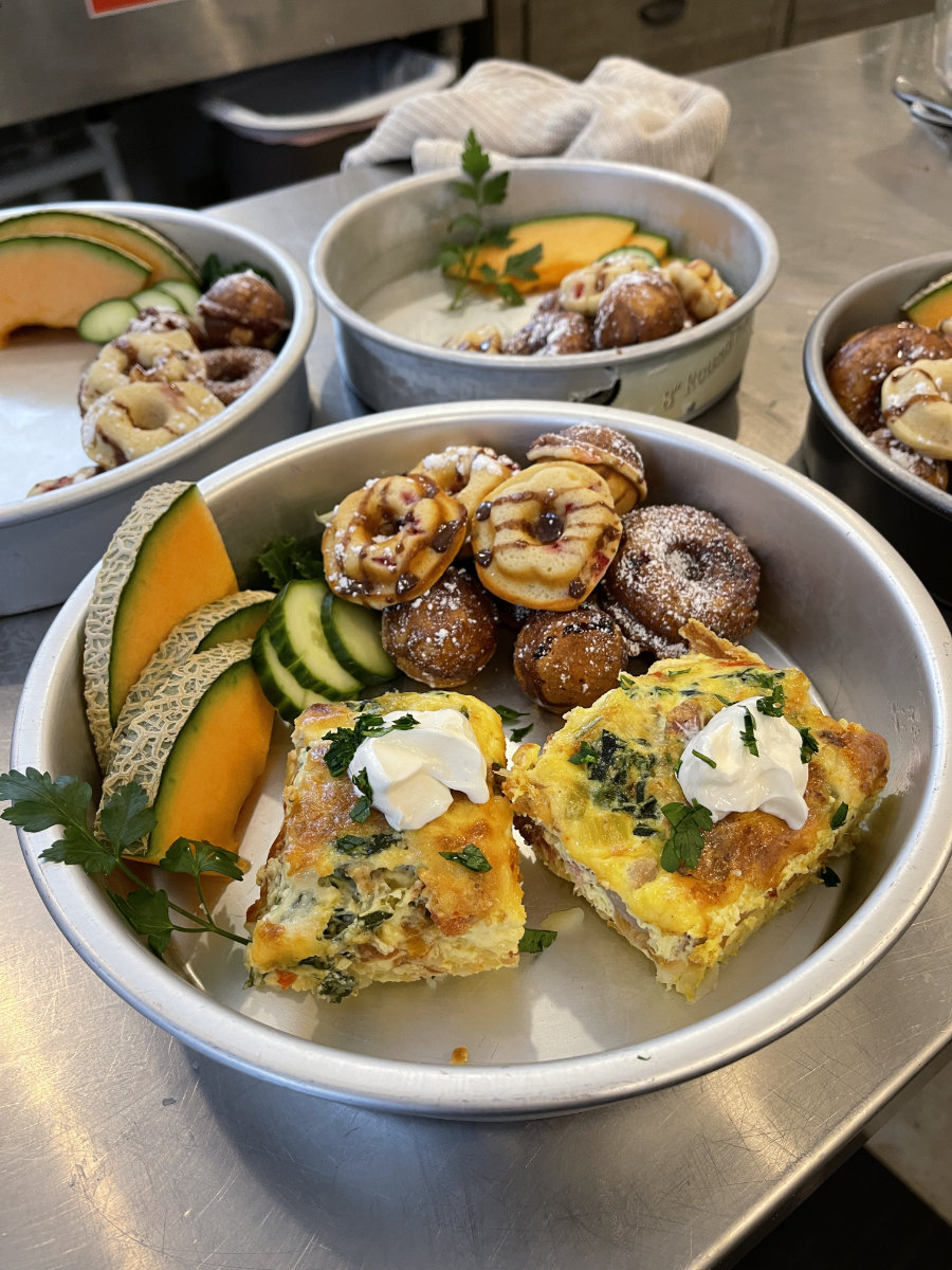 Hash brown quiche filled with home grown veggies, homemade baked doughnuts, and sliced melon and cucumber ready to be served as room service.