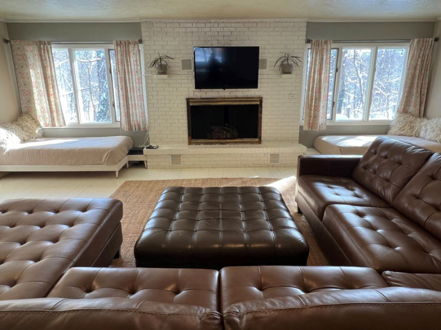 Large living room sectional leather sofa with gas fireplace, two daybeds, astreaming tv, and views of the river and woods below.