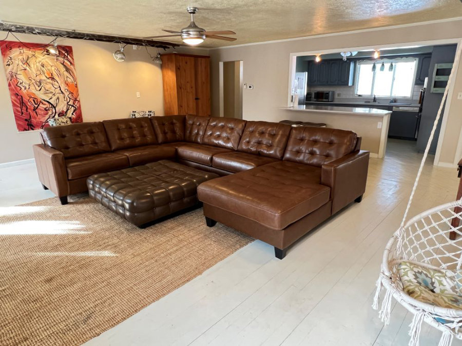 Large leather sectional sofa with attached kitchen. The room is decorated with original art, funky light fixtures, and a hanging chair.