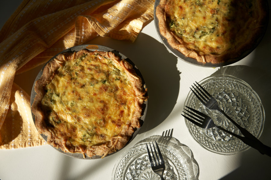 Two quiches, plates, and forks sit on a table is glowing sunlight.