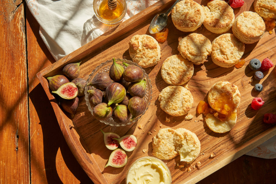 Homemade biscuits, some covered in jelly, Goldberry grown figs, and berries cover a tray.