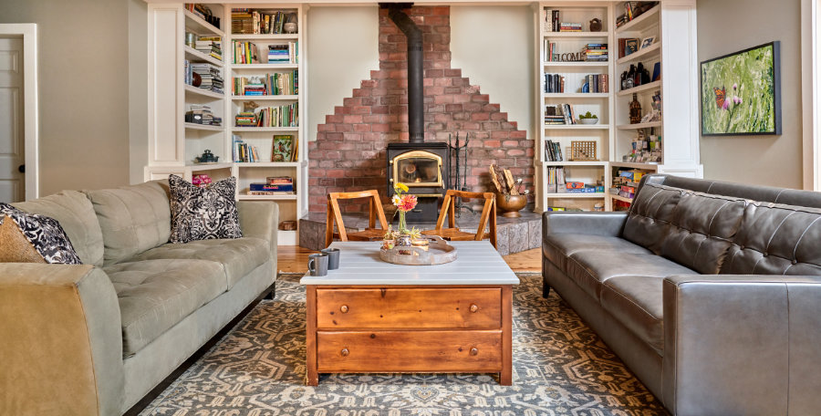 Living Room with sofas and chairs for guests to use along with bookcases full of games, puzzles, books, and information on things to do in the area. In the background, you can see the large, brick wood-burning fireplace.
