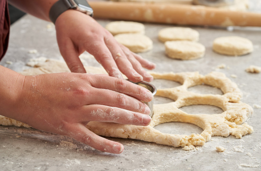 Hands use a biscuit cutter to cut circles out of dough.