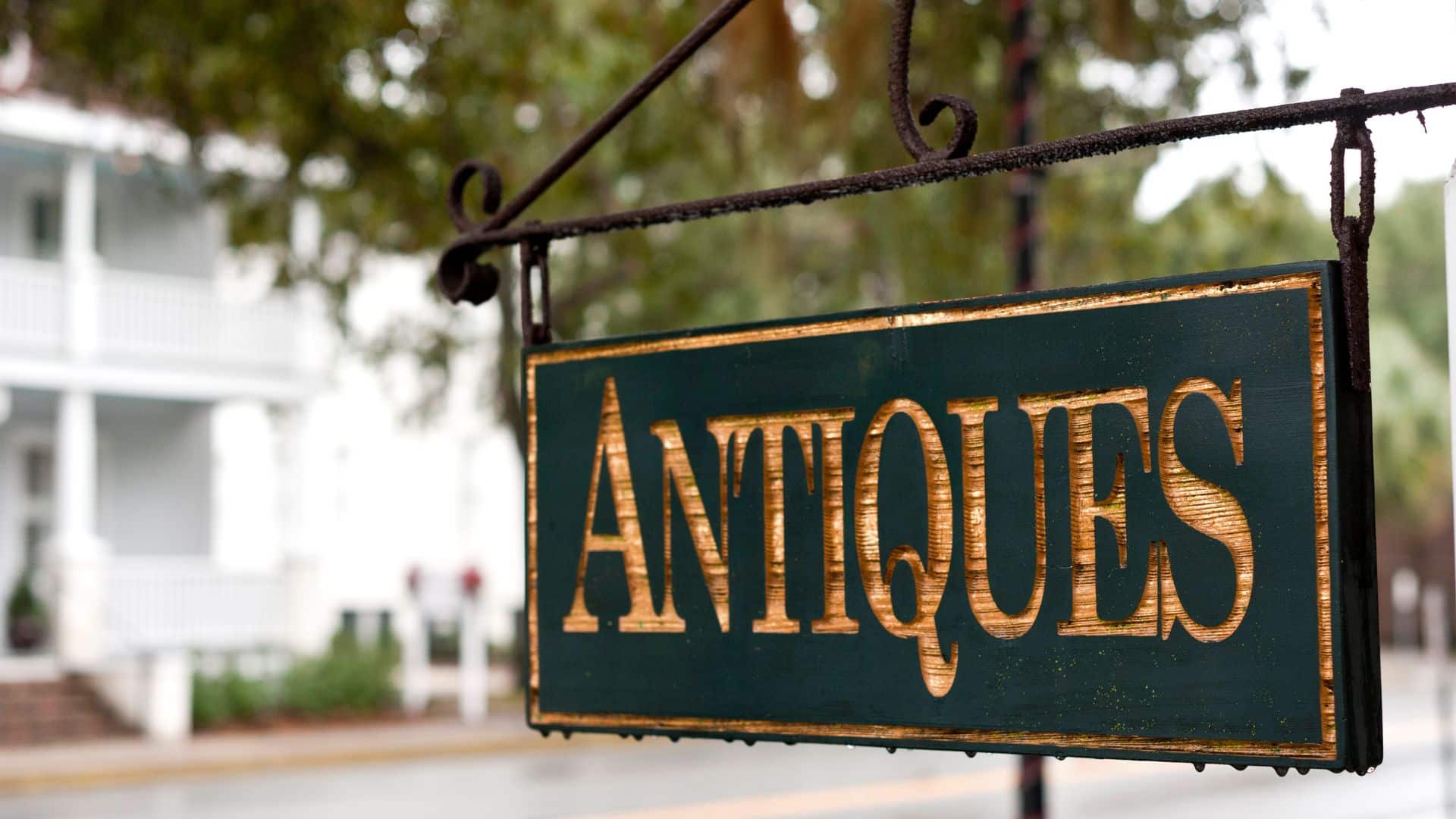 wooden antiques sign with gold lettering hanging on an iron post