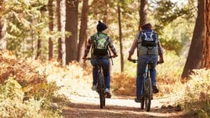 couple riding a bike trail surrounded by foliage that is still transitioning from greens to golds and browns