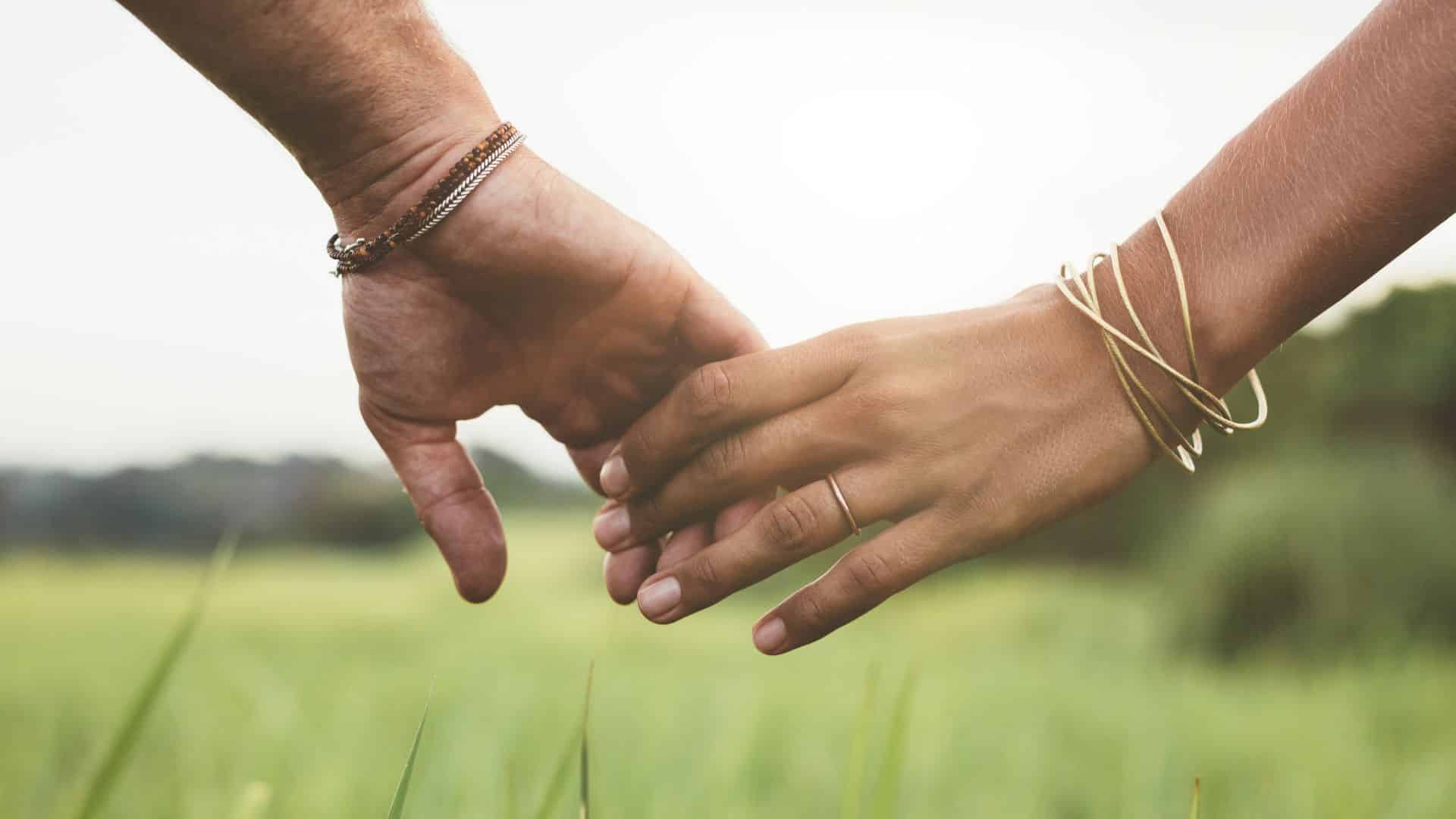 close-up of couple holding hands with blurred backdrop of grass blades, field, and outcroppings