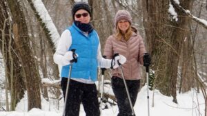 julie and guest smiling while snowshoeing through the woods