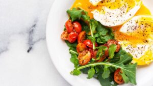 two soft boiled eggs next to spring greens and halved grape tomatoes