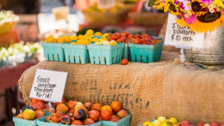 pints of tomatoes and a metal bucket of fresh flowers displayed on a stand at a farmers market