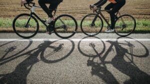 midsection down of two cyclists riding bicycles riding a lined paved route next to a field