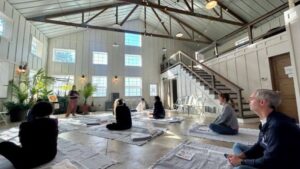 a wellness retreat class hosted at goldberry woods with participants seated on rugs on the floor with legs folded in a meditative pose
