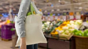 woman shopping with a tote filled with a water bottle and fresh produce