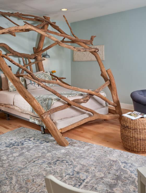 A guestroom painted in a soft blue. with a stunning bed made from enormous driftwood logs from a lake.