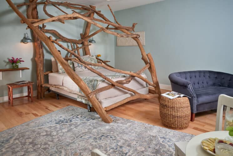 A guestroom painted in a soft blue. with a stunning bed made from enormous driftwood logs from a lake.