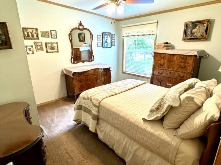 A bedroom with a bed with tan bedding, a quilt t the foot of the bed, and antique dressers.
