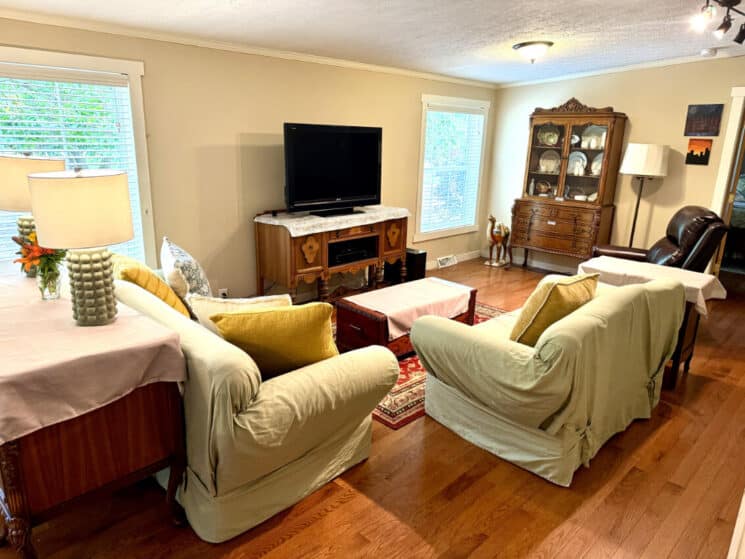 A living room with a covered sofa and loveseat, a reclining chair, a china hutch, and a flat screen TV.