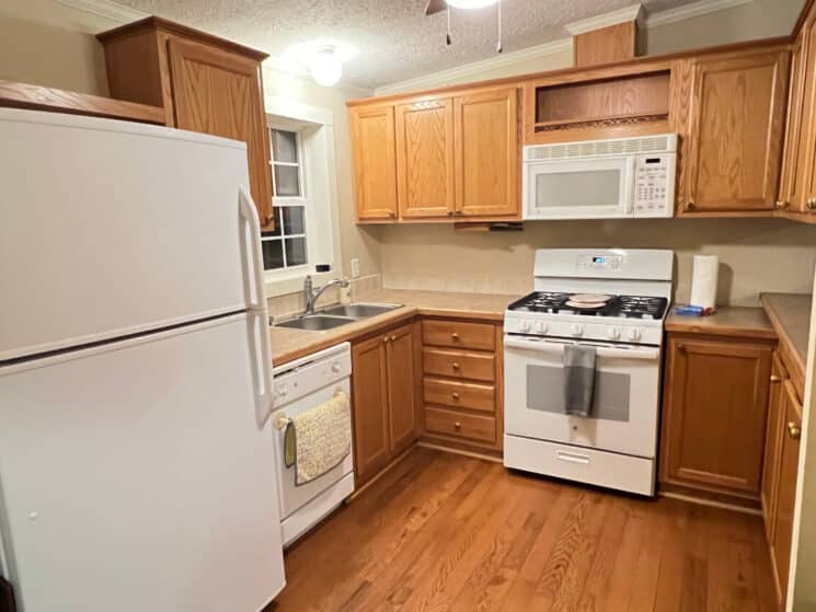A kitchen with wood cupboards, wood floors, and white appliances including a fridge, dishwasher, microwave and stove and oven.