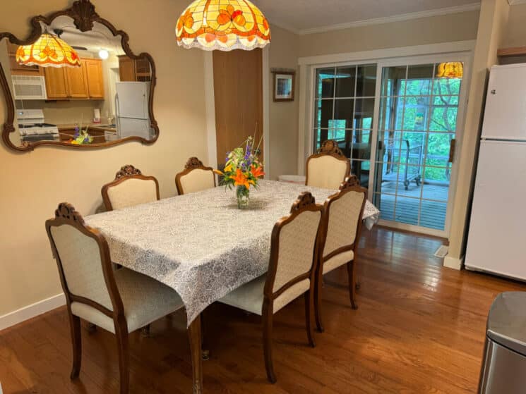 A dining room with wood floors, a dining table covered with a white tablecloth and 6 chairs, and sliding doors going out to a patio.
